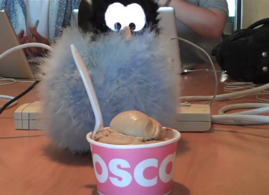 small fluffy robot on a table looking at a bowl of ice cream