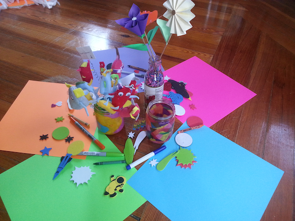 five colorful sheets of scrapbook paper arranged in a circle on the floor, with several jars in the middle containing a candle and paper flowers, with scrapbook materials scattered around