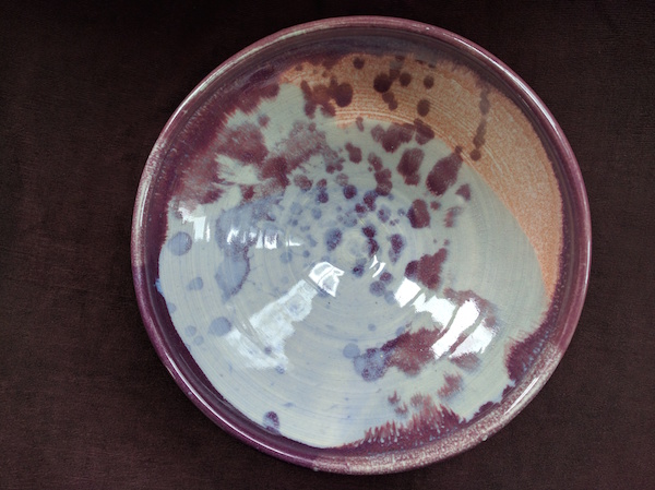 top down view of a bowl with a purple rim and purple spots on top of pale blue and a streak of pinkish red