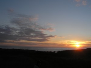 yellow sun setting over dark hills and navy water, faded sunset