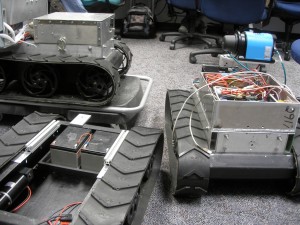 three metal boxy robots with treads
