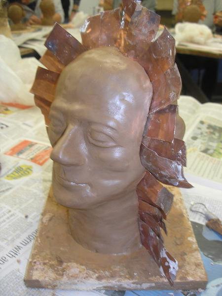 clay head with thin metal pieces inserted across the crown of the head and down in front of the ears