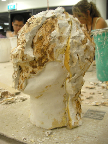 with part of the layers of plaster removed, the neck and chin of the casting is visible