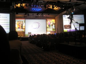 _large conference room, stage lit up at the front with one of the grace hopper conference speakers_