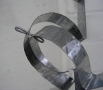 A wire is threaded through a hole in each of two steel puzzle piece frames and bent over on either end to hold the frames together