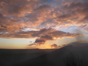 pink clouds on a pastel sky, smoke rising below from a volcano, lit from the last sunlight of day