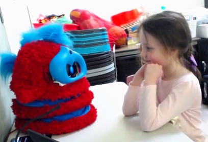 A girl smiles at a red and blue fluffy robot