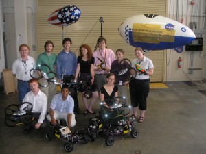 group shot of nine interns and Garry (one intern, Leo, is not pictured) in front of blimps, holding quadcopters and shiny cars