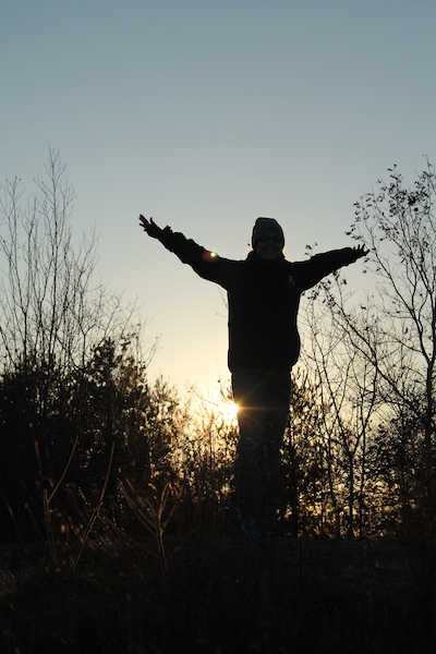 silhouette of person standing with arms raised in front of setting sun