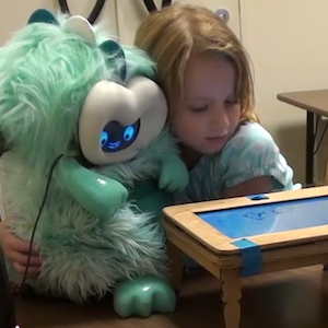 a young girl hugging a fluffy dragon robot behind a little play table
